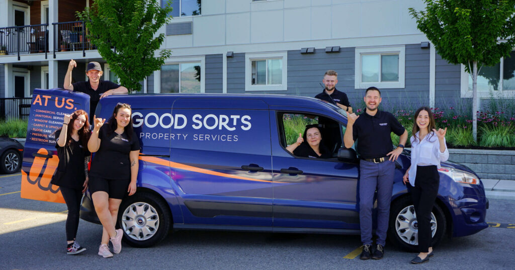 The Good Sorts Property Services team with the hang loose hand gesture and in uniform standing outside in front of the Good Sorts company van, a professional cleaning team offering commercial cleaning and janitorial services in Kelowna and the Okanagan.