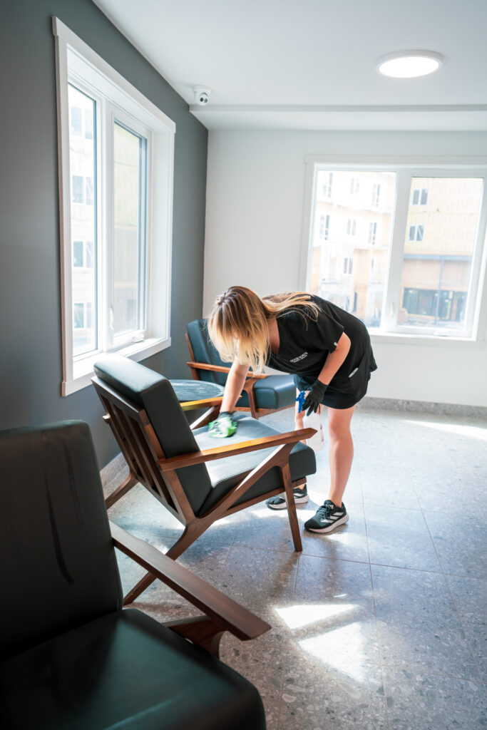 Good Sorts cleaning crew member wiping down chairs in office with green cloth
